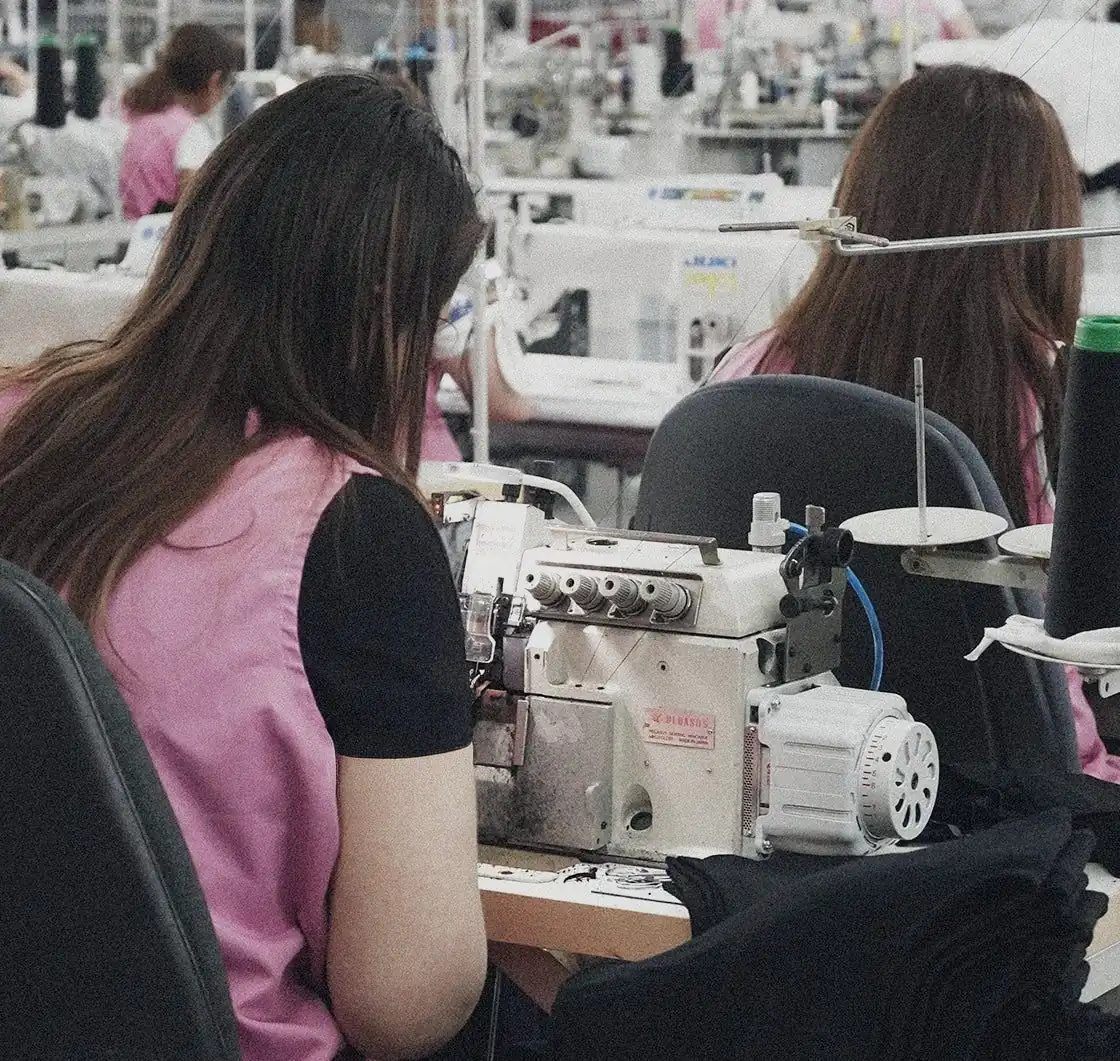 Personas cosiendo prendas negras en máquinas remalladoras