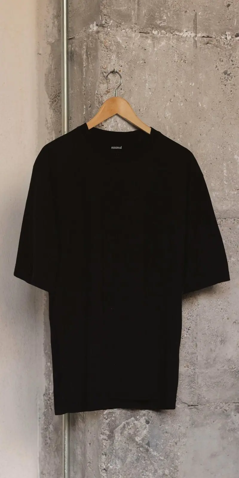 La camiseta negra de algodón orgánico en una percha de madera, contra una pared de hormigón