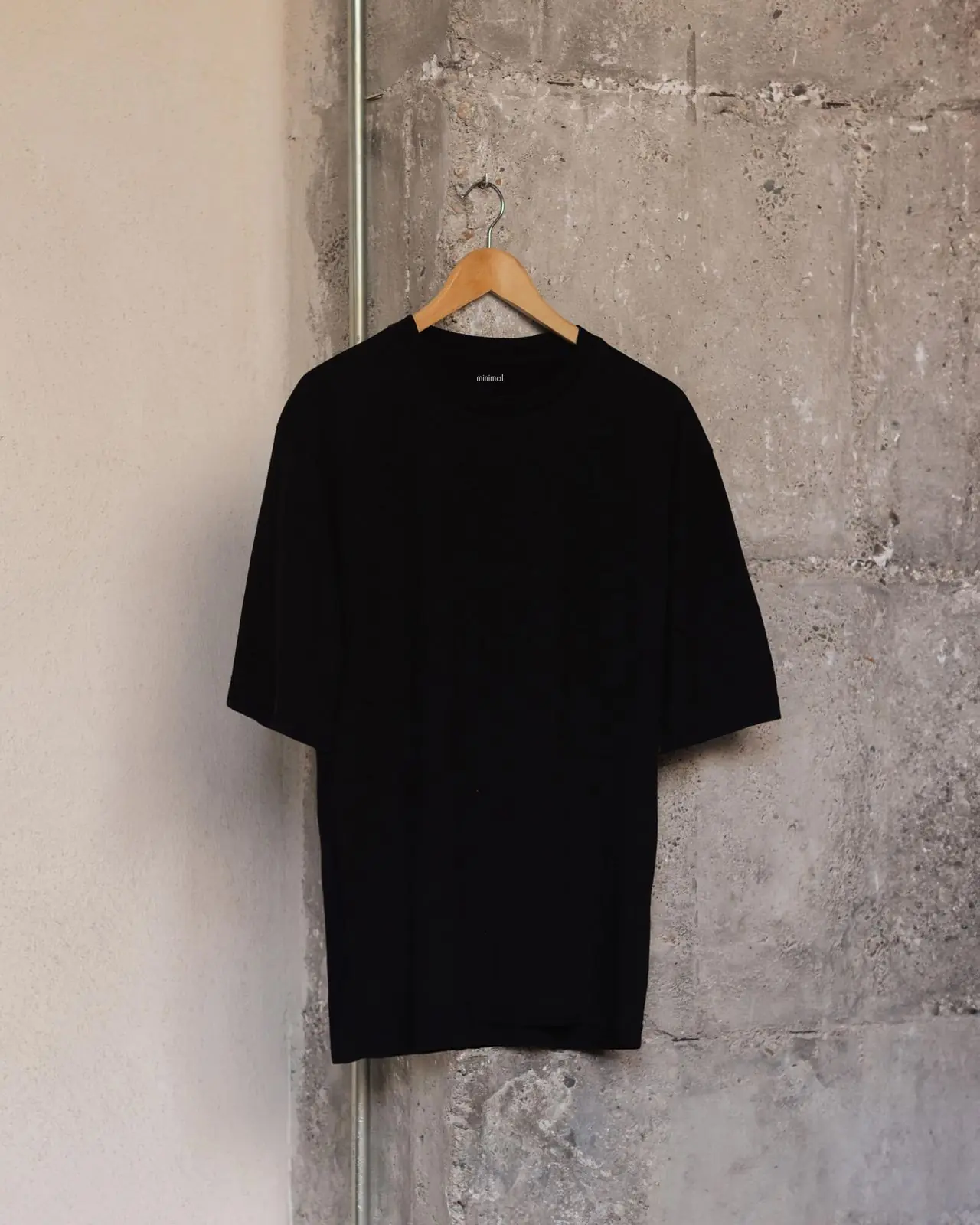 La camiseta negra de algodón orgánico en una percha de madera, contra una pared de hormigón