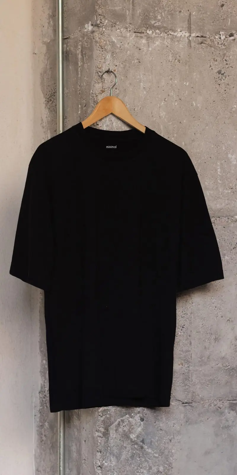 La camiseta negra de algodón orgánico en una percha de madera, contra una pared de hormigón